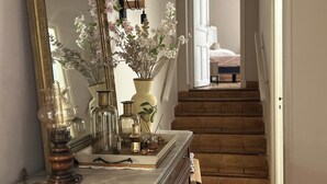 A hallway with a large ornate mirror, a wooden dresser, and a staircase leading to another room.