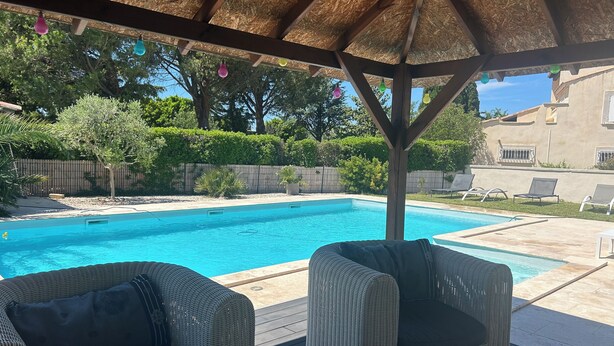 A covered outdoor area with a pool, wicker furniture, and a thatched roof.