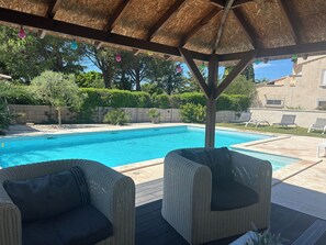 Ett takförsett utomhusområde med en pool, möbler av rotting och ett halmtak.