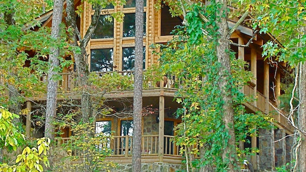 Une cabane en rondins à plusieurs niveaux, entourée d’arbres et dotée de grandes fenêtres.