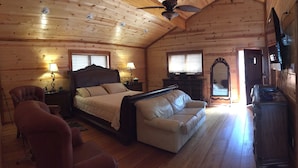 Une chambre confortable dans un chalet en rondins, avec un grand lit, deux fauteuils, un canapé et une commode en bois.