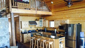 Une cuisine spacieuse avec des meubles en bois, un grand îlot central doté de tabourets, un réfrigérateur en acier inoxydable et un ventilateur de plafond.