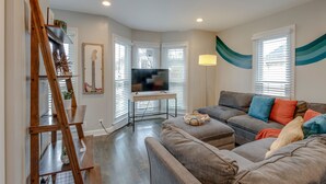 Un salon avec un canapé gris, une échelle en bois, un téléviseur posé sur un meuble et une lampe.
