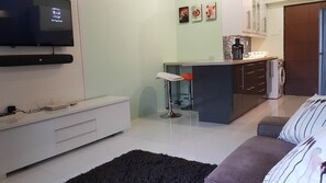 A modern living room with a flat-screen TV, a sofa, a coffee table, and a kitchen area with a washing machine.