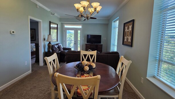 A dining area with a round table, four chairs, a chandelier, and a television in the background. - Luxury Condo! 4 Miles To Dollywood, Easy Walk To Shops & Restaurants (Pigeon Forge)