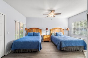 A bedroom with two beds, a ceiling fan, and a window with blinds.