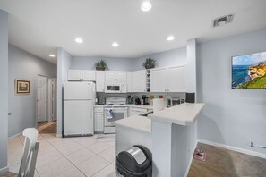 A compact kitchen with white cabinets, a refrigerator, a microwave, and a sink. There is a small island with a countertop and a trash can.