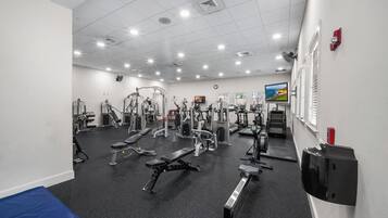 A gym with various exercise equipment, a clock on the wall, and a television screen.