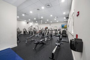 A gym with various exercise equipment, a clock on the wall, and a television screen.