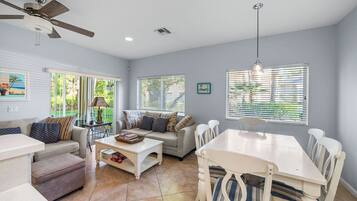 A spacious living area with a ceiling fan, a dining table with chairs, a sofa with cushions, and a coffee table.