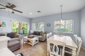 A spacious living area with a ceiling fan, a dining table with chairs, a sofa with cushions, and a coffee table.