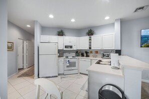 A modern kitchen with white cabinetry, a built-in oven, microwave, and a sink. There is a small island with a sink and a trash can. - PGA Village/Castle Pines Best Location Pet Friendly. (Port St. Lucie)