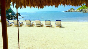 Une plage avec des chaises longues blanches sous un toit de chaume, donnant sur l’océan.