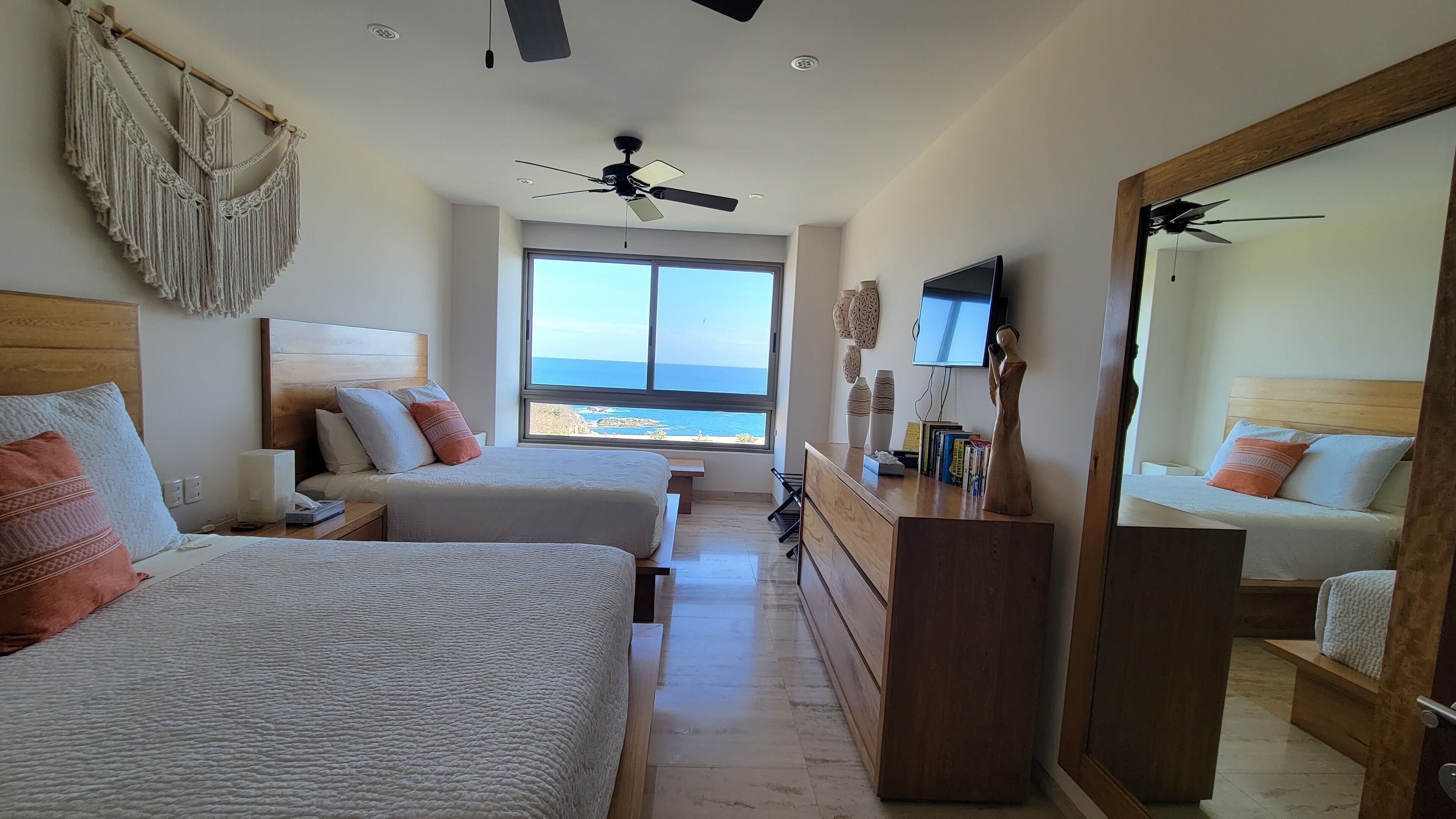A bedroom with two beds, a dresser, a TV, and a view of the ocean.