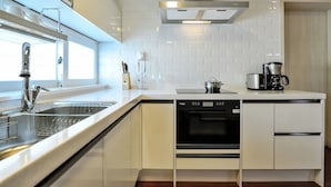 A modern kitchen with white cabinetry, a stainless steel sink, a built-in oven, and a coffee maker. - Aquarius resort (Geoje)