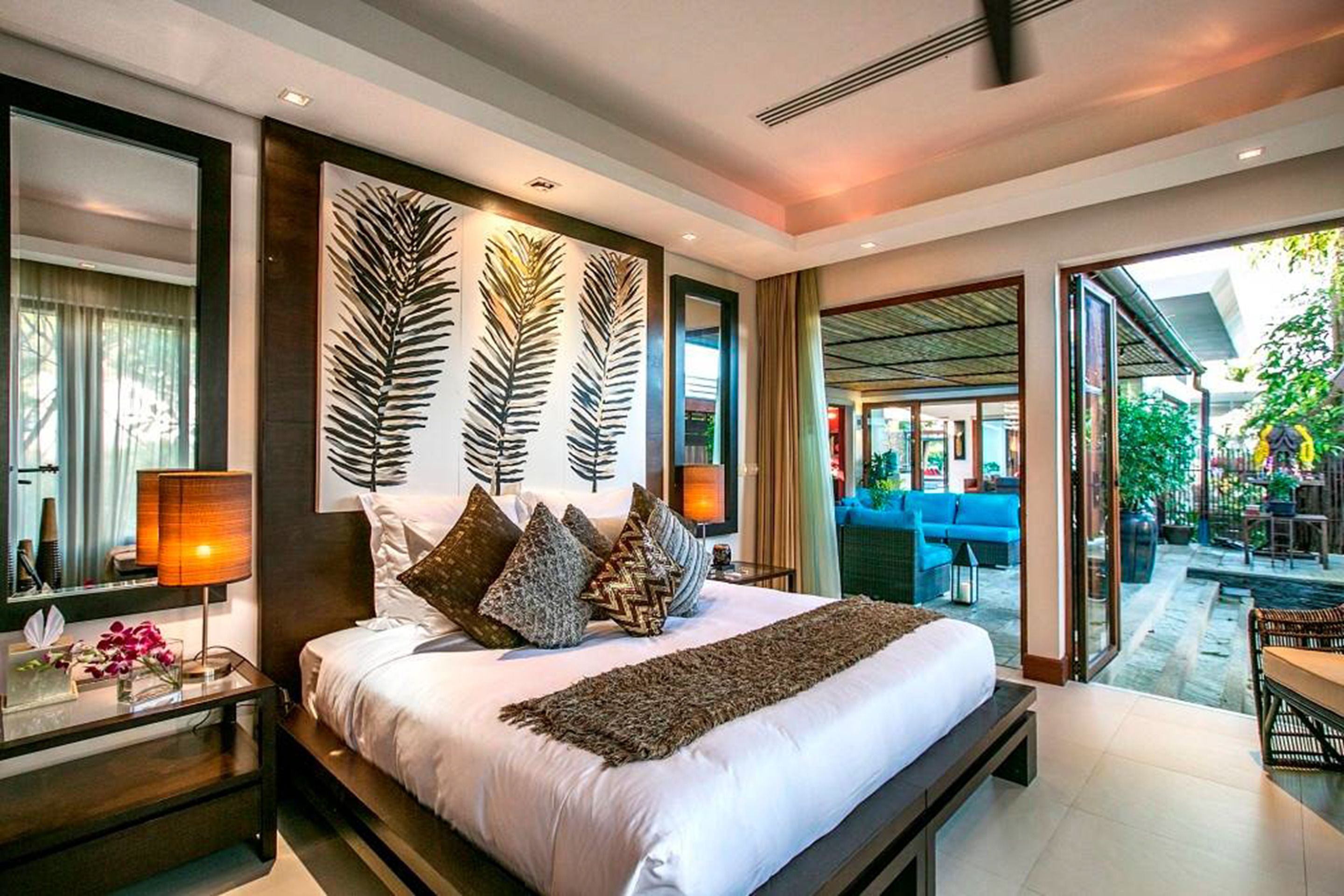 A modern hotel bedroom with a large bed, a nightstand, and a view of the outdoor seating area.