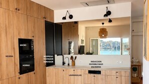 A modern kitchen with labeled cabinets, a dining area with a glass table, and a view of the outdoors.