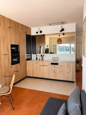 Una cocina moderna con armarios identificados, un comedor con mesa de vidrio y vistas al exterior.