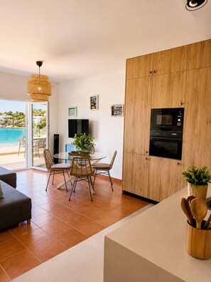 A modern kitchen with a built-in microwave and oven, a dining area with wicker chairs, and a view of the sea through large windows.