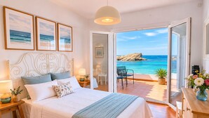 A bedroom with a bed, bedside tables, a nightstand, a lamp, a dresser, a window with a view of the sea, and a ceiling light.