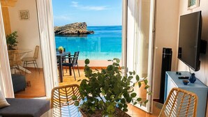 A dining area with a glass table, wicker chairs, and a view of the sea.
