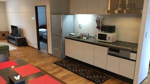 Una cocina moderna con microondas integrado, refrigerador de acero inoxidable y lavavajillas. Hay una mesa de madera con un mantel individual rojo y una caja de pañuelos.