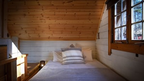 A small, cozy room with wooden walls and a sloped ceiling. There is a bed with pillows and a lamp on a nightstand. - Beaver Lodge Hakuba (Hakuba)