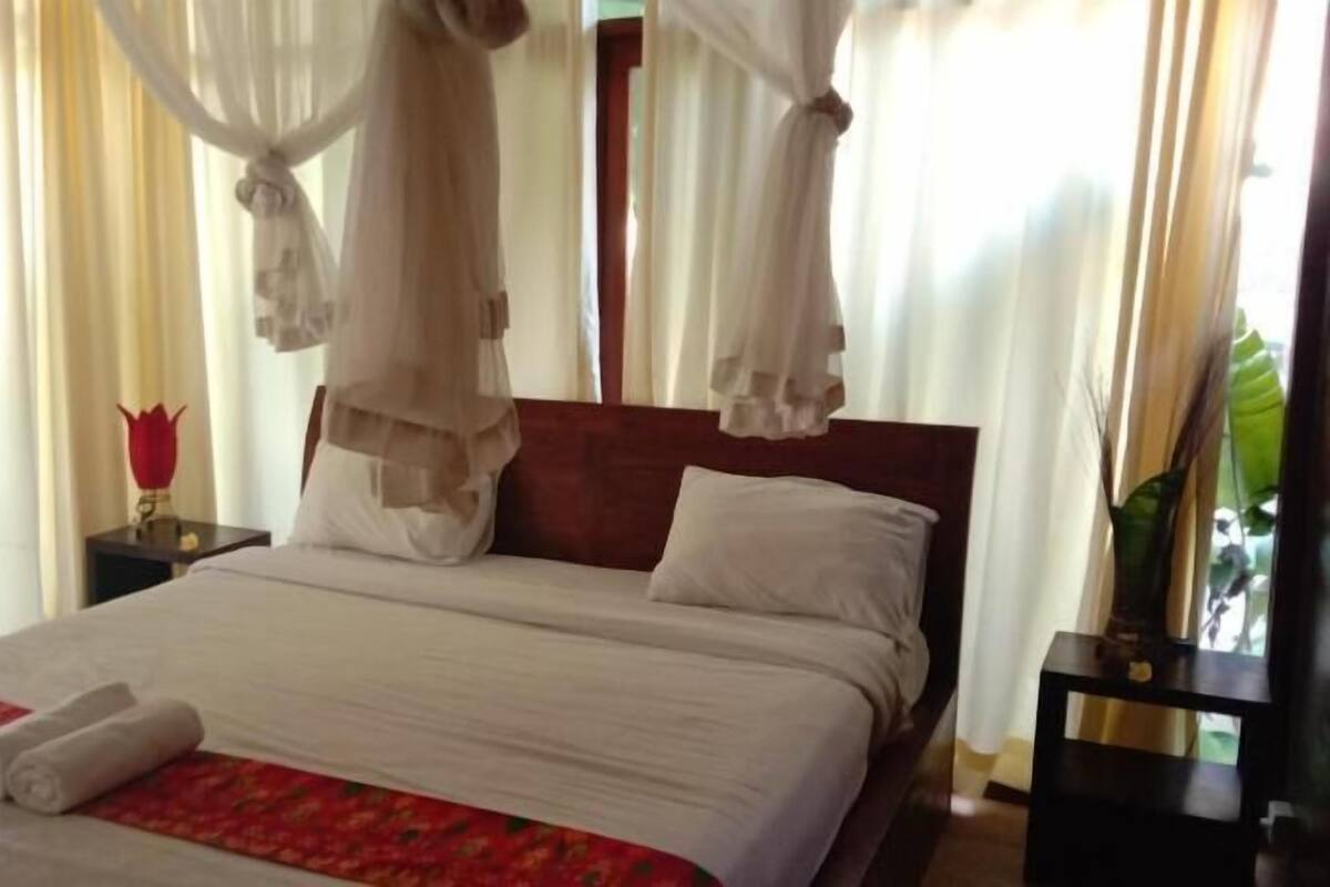 Ein Bett mit weißen Leinen, einer roten Blütenfloralen Tagesdecke und einem Baldachin.