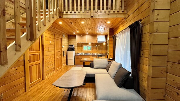 Een interieur van een chalet met een houten trap, een keukenhoek, een bank en een eettafel.