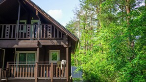 Een chalet met een houten terras en veranda, omgeven door dicht bos.