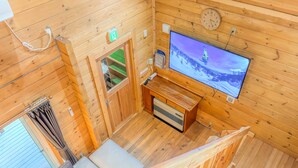 Een houten hutje met een televisie waarop een besneeerd landschap te zien is, een houten bankje en een kleine tafel met een afstandsbediening.