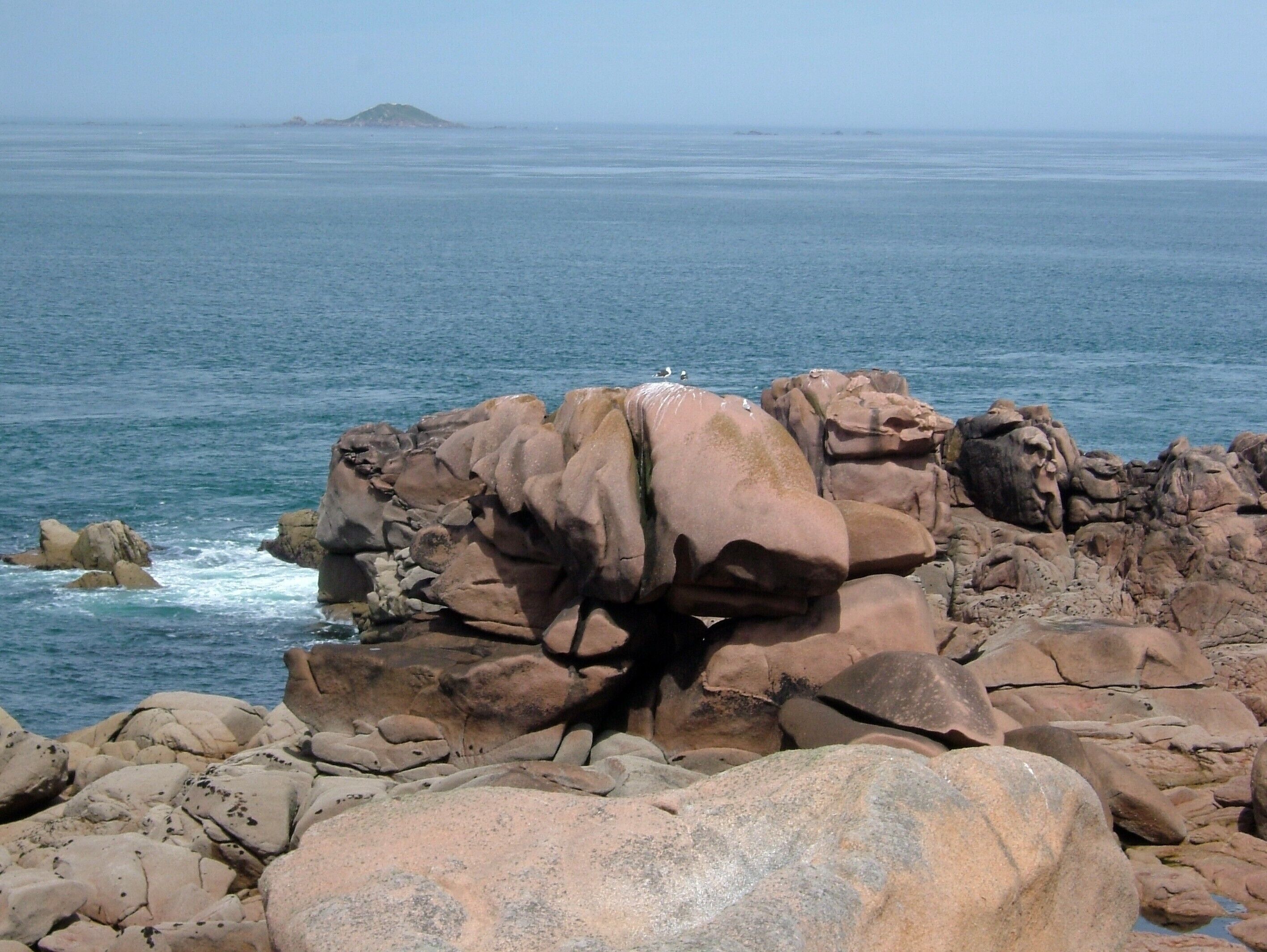 A rocky coastal landscape with large boulders and a clear view of the ocean.