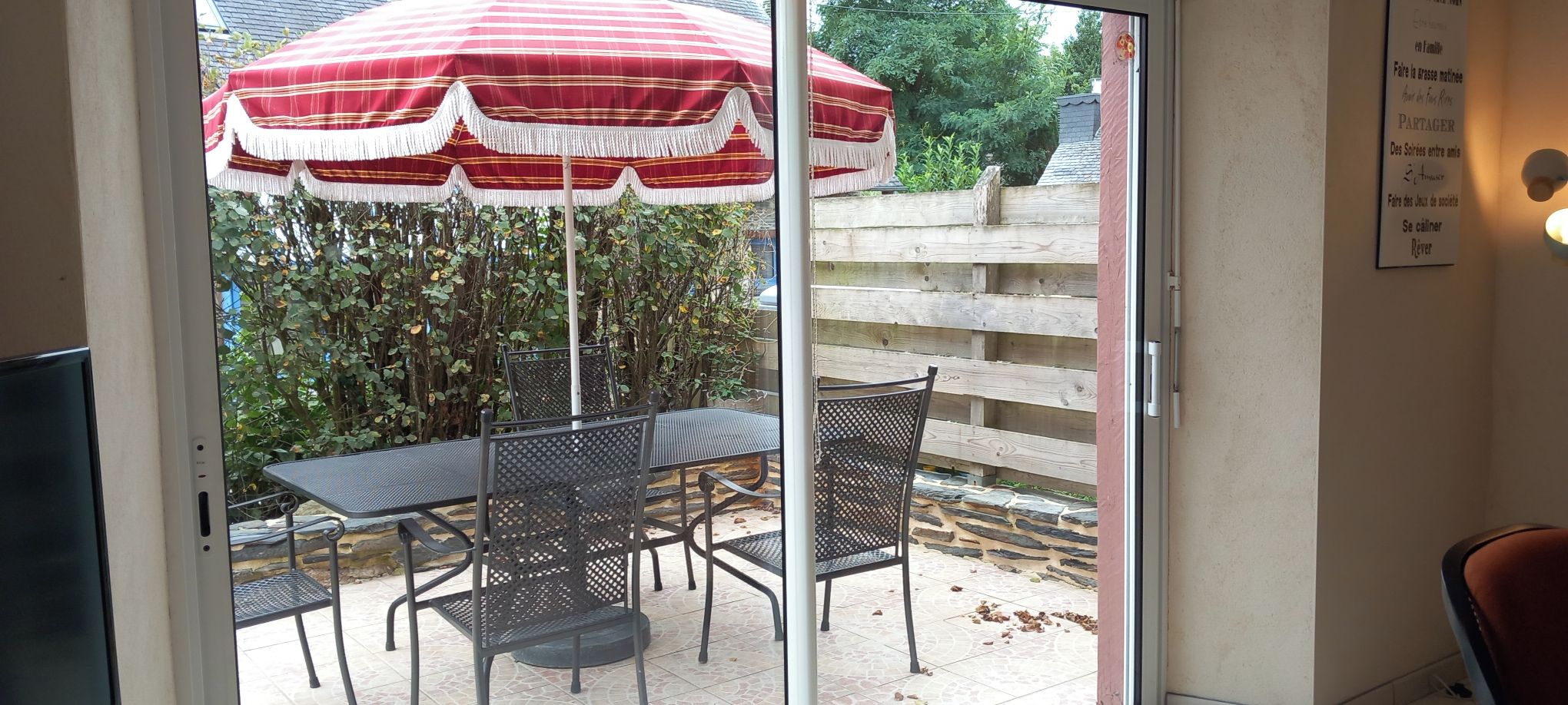 A patio area with a table and chairs, a red and white striped umbrella, and a wooden fence in the background.