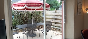 A patio area with a table and chairs, a red and white striped umbrella, and a wooden fence in the background.
