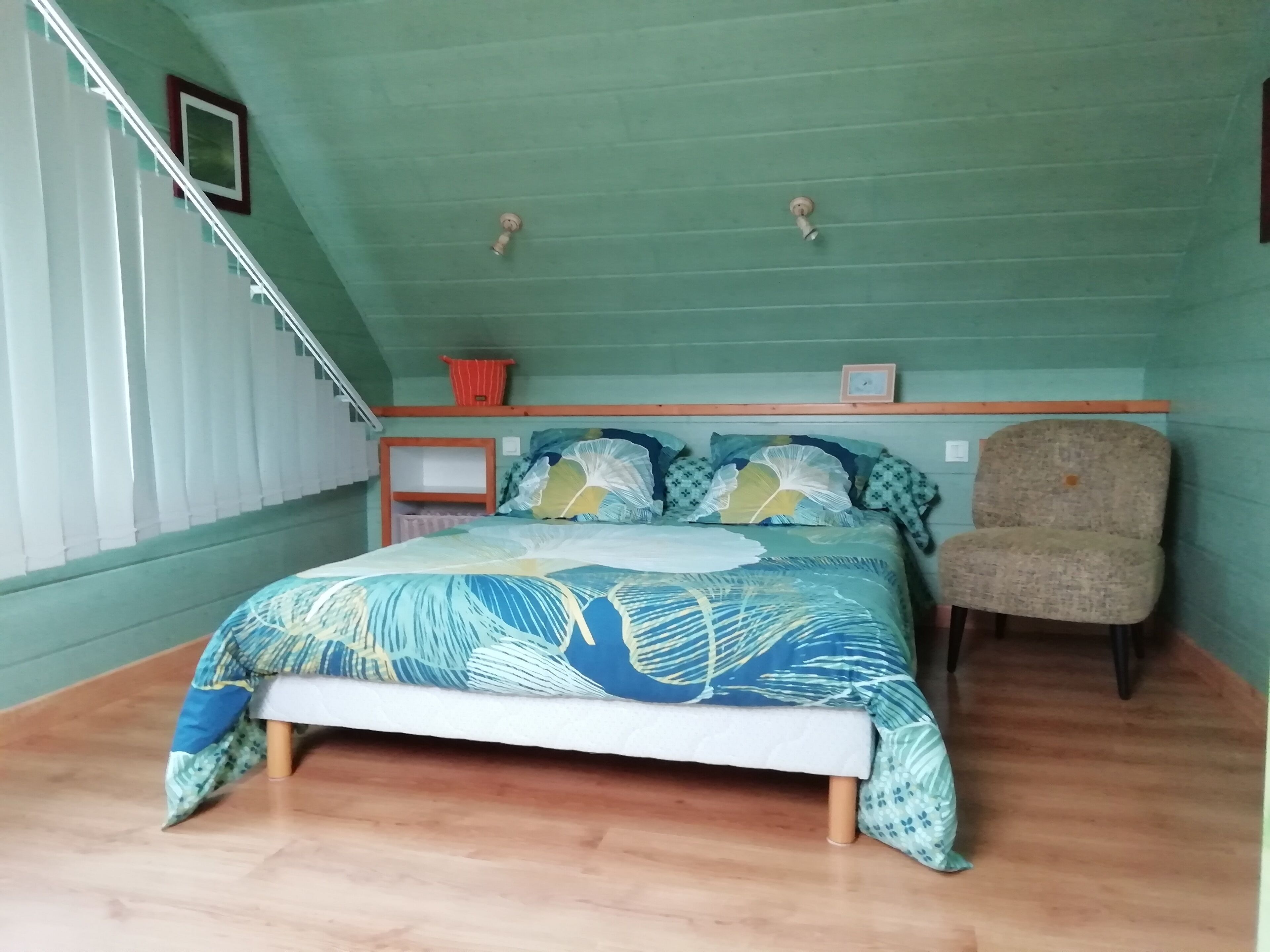 A bedroom with a bed, a chair, a shelf, and a window with blinds.