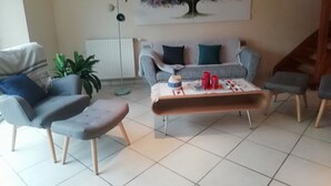 A living room with a grey sofa, a coffee table with red cups, and a colorful tree painting on the wall. - House in Breton village between land and sea (Le Cloitre Saint Thegonnec)