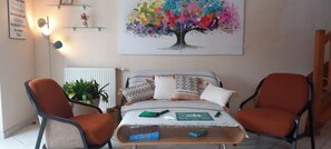 Ein Wohnzimmer mit einer Couch, zwei Sesseln, einem Couchtisch und einem Gemälde eines bunten Baumes.