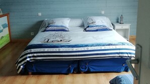A bedroom with a sloped ceiling, a bed with a nautical-themed bedspread, two wall-mounted brass light fixtures, and a small white nightstand with a decorative item. - House in Breton village between land and sea (Le Cloitre Saint Thegonnec)
