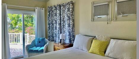 A bedroom with a large bed, a chair, a nightstand, and a window with curtains.