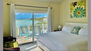 A bedroom with a bed, a painting, and a view of the ocean.