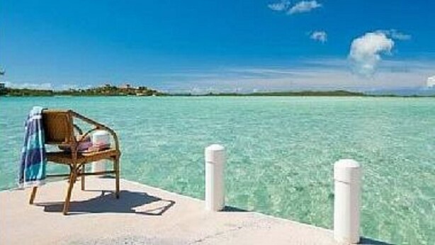 A wooden chair on a concrete platform with clear turquoise water and a distant shoreline.