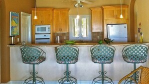 A kitchen with wooden cabinets, a microwave, an oven, a refrigerator, and a bar area with four chairs.