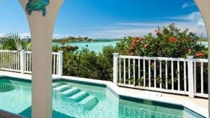 A pool with clear blue water, surrounded by a white fence and lush greenery.