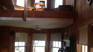 A cabin interior with a dining area, a loft with a chair, and a kitchen area.