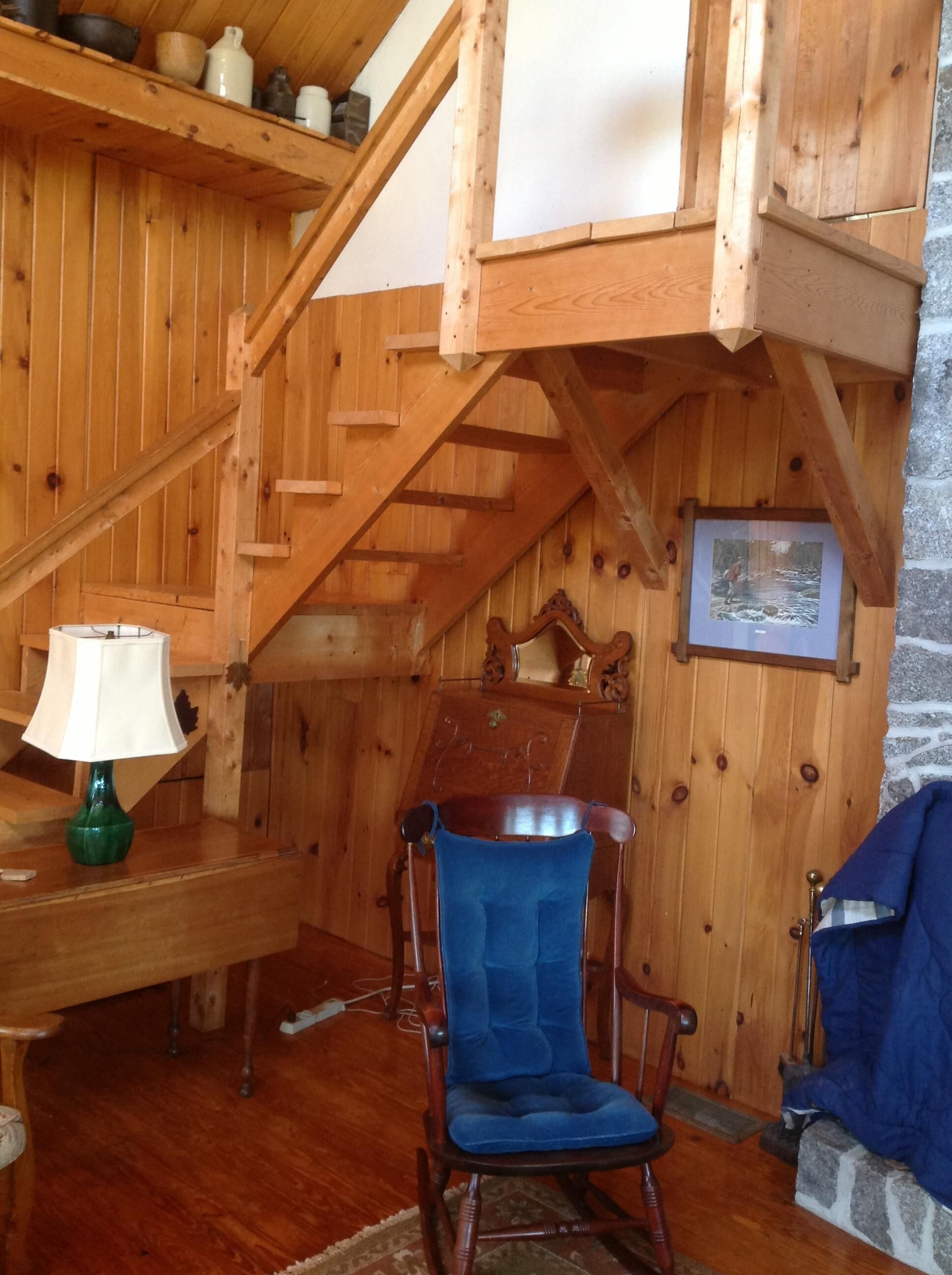 Un interior de madera con una mecedora, una lámpara y una escalera.