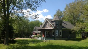 A two-story house with a porch, surrounded by a grassy yard and trees.