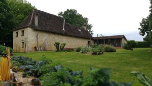 Un edificio de piedra con tejado de tejas, rodeado de un césped y jardín bien cuidados.