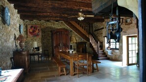 Un interior rústico con una mesa de madera, bancos, una escalera y paredes de piedra.