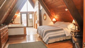 Een gezellig slaapkamer onder het dak met een groot bed, een houten dressoir en een badkamer met bad.