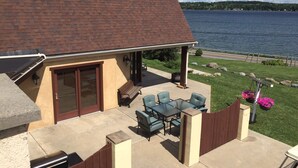 Een terras met een tafel, stoelen, een barbecue en uitzicht op een meer.
